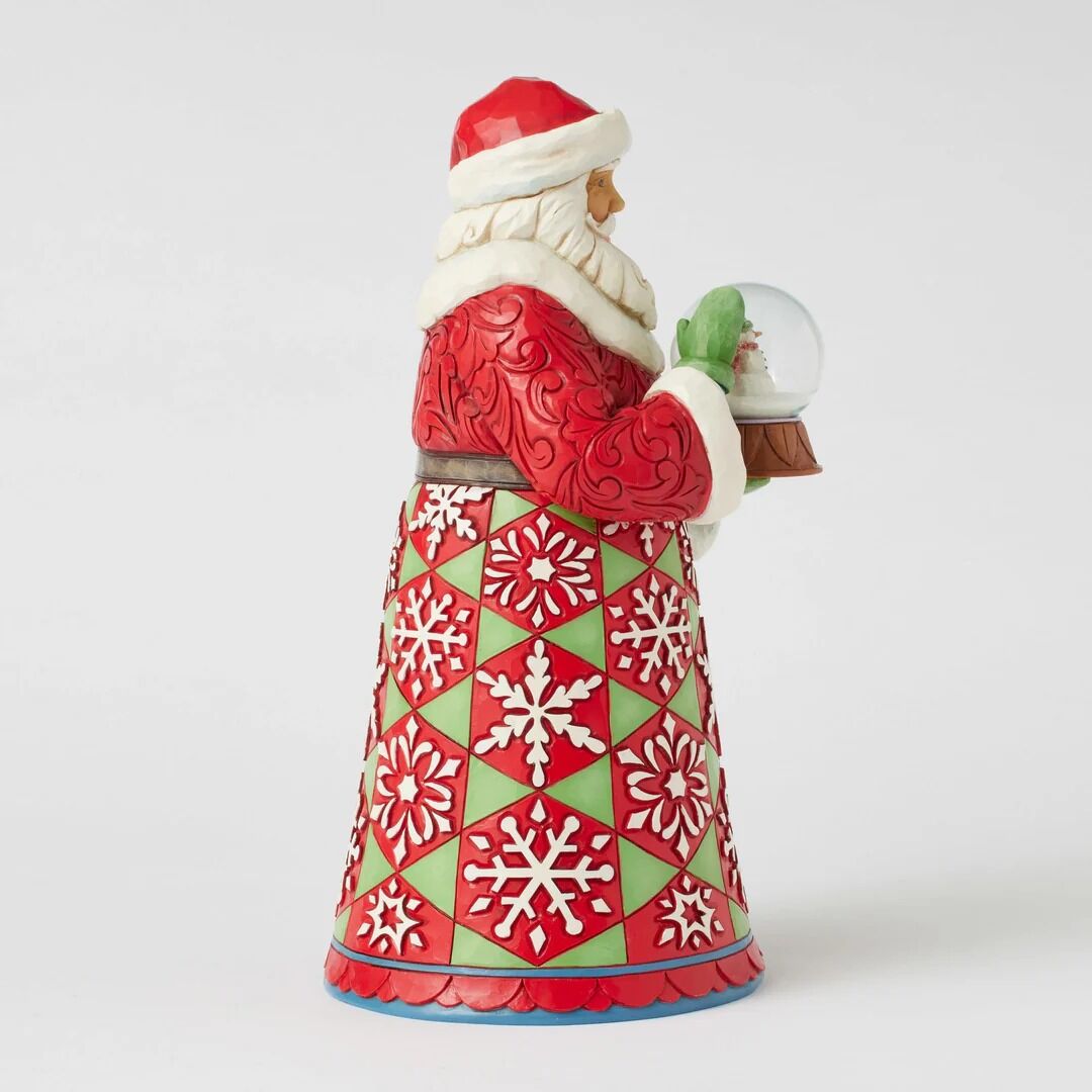 A Santa Claus figurine wearing a red and green patterned robe with white fur trim, holding a small snow globe, photographed on a clean light gray background.