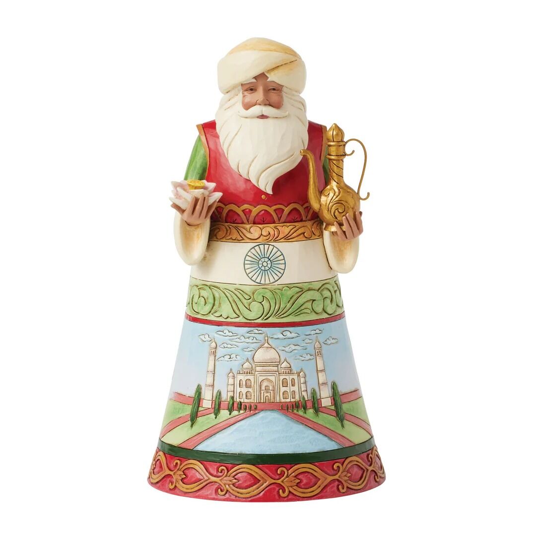 A Santa Claus figurine decorated with traditional Indian attire, featuring a white turban and beard, holding a small bowl and a gold-colored pitcher. The lower portion of the dress is illustrated with a view of the Taj Mahal under a blue sky.