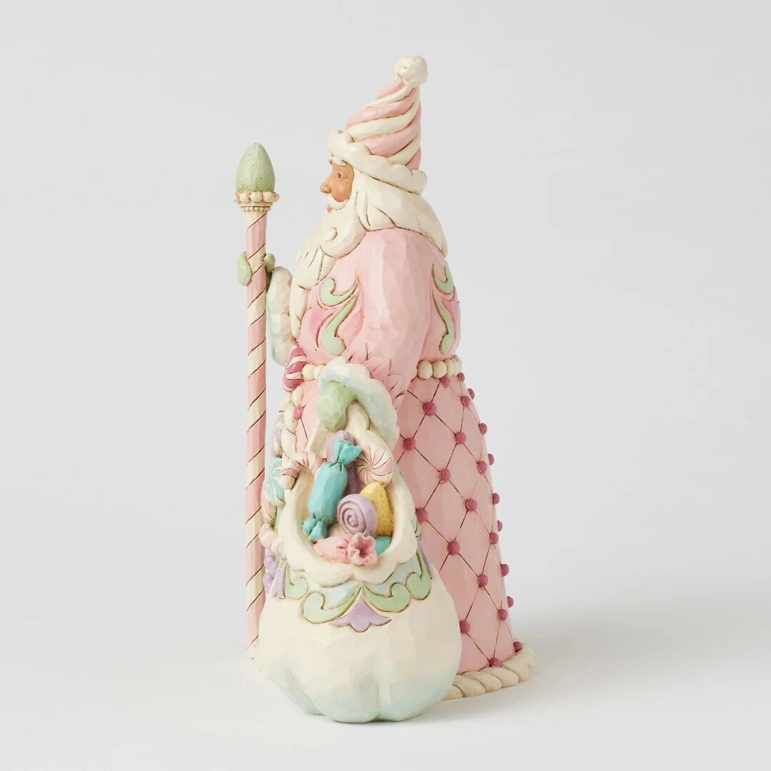 A whimsical Santa Claus figurine in pastel pink and cream, holding a striped pole and a basket of colorful candy, photographed against a clean light gray background.