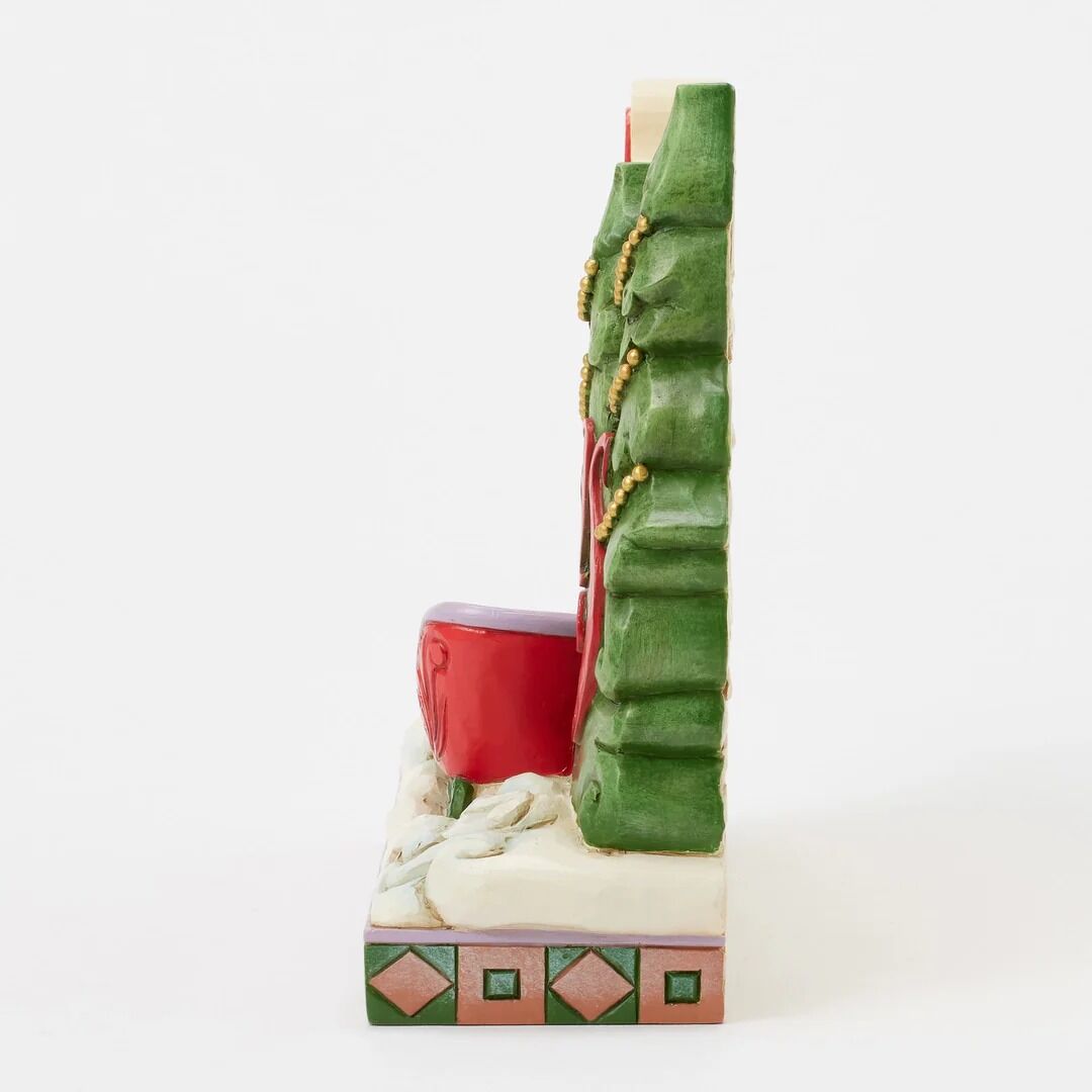 A decorative ceramic Christmas-themed bookend featuring a green pine tree, a red mug, and a white snowy base with geometric patterns.