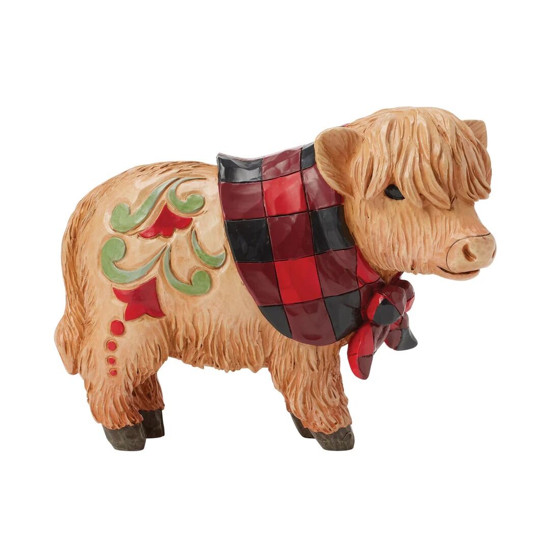 A Highland cow figurine with shaggy tan fur, decorated with green and red scrollwork on its side and a red and black checkered scarf with a matching red bow, shown against a plain white background.