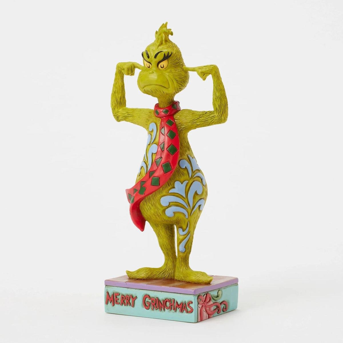 A collectible figurine of the Grinch flexing his biceps, wearing a red and green patterned tie and a blue and white patterned vest, standing on a light blue base that reads 'MERRY GRINCHAS'.