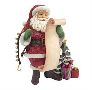 Decorative figure of Santa Claus holding a list with a gift bag and tree in the background.