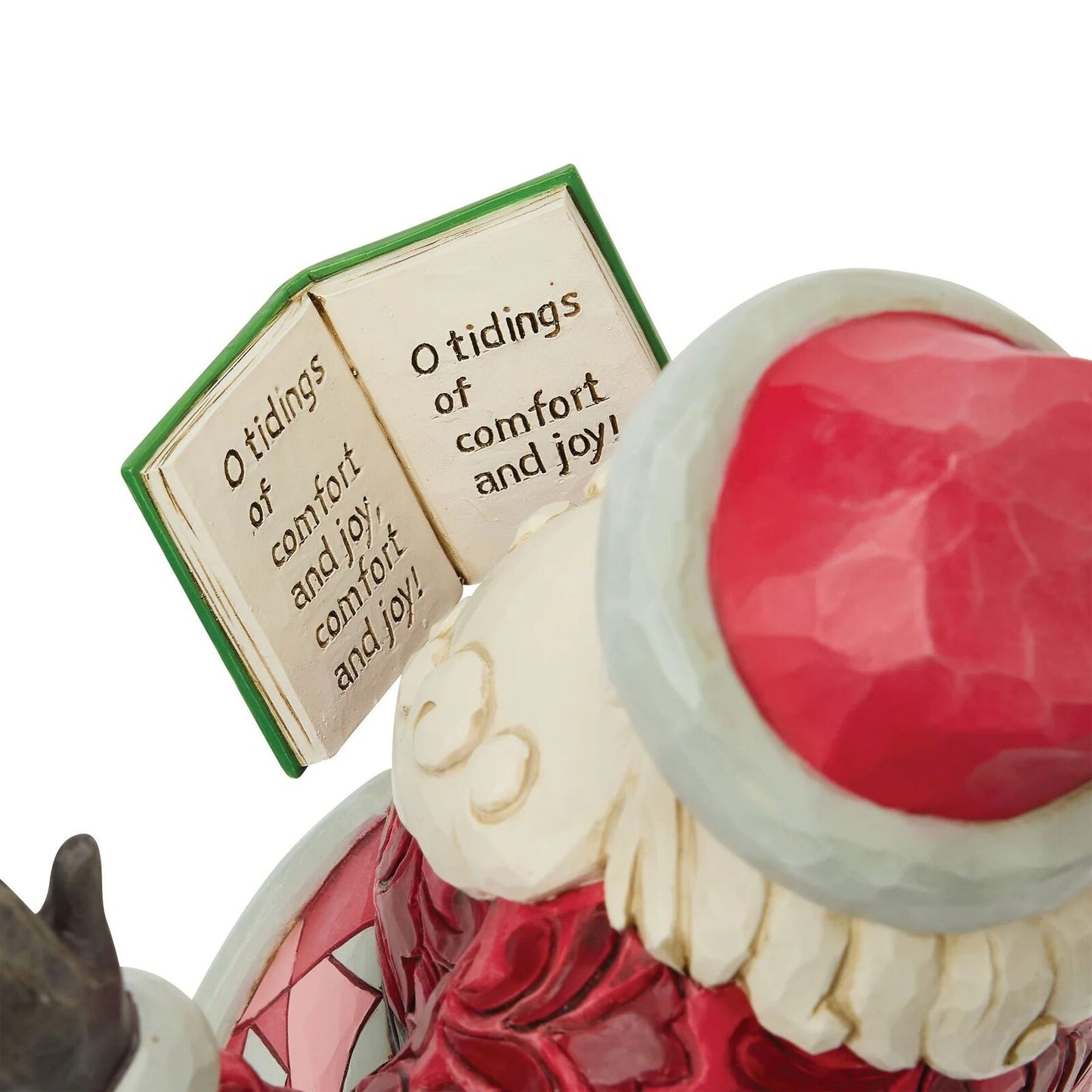 A close-up of a Santa Claus figurine showing part of his red hat, white beard, red coat, and an open book with the quote 'O tidings of comfort and joy!'.