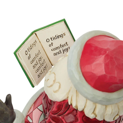 A close-up of a Santa Claus figurine showing part of his red hat, white beard, red coat, and an open book with the quote 'O tidings of comfort and joy!'.
