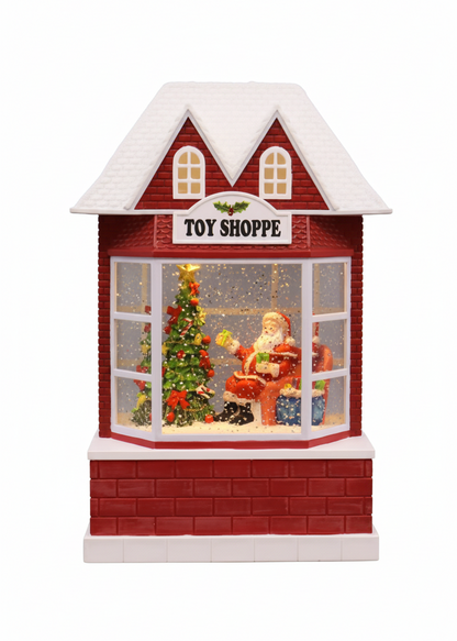 A red and white toy shop window decoration with a snowy roof, a Christmas tree, and Santa Claus sitting inside, labeled 'TOY SHOPPE' on the front.