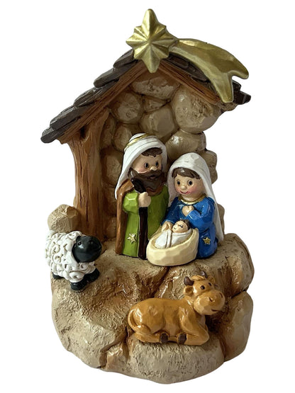 A painted resin Christmas nativity scene figurine featuring Mary, Joseph, baby Jesus in a manger, a sheep, and a cow, set under a stable with a gold star on a white background.