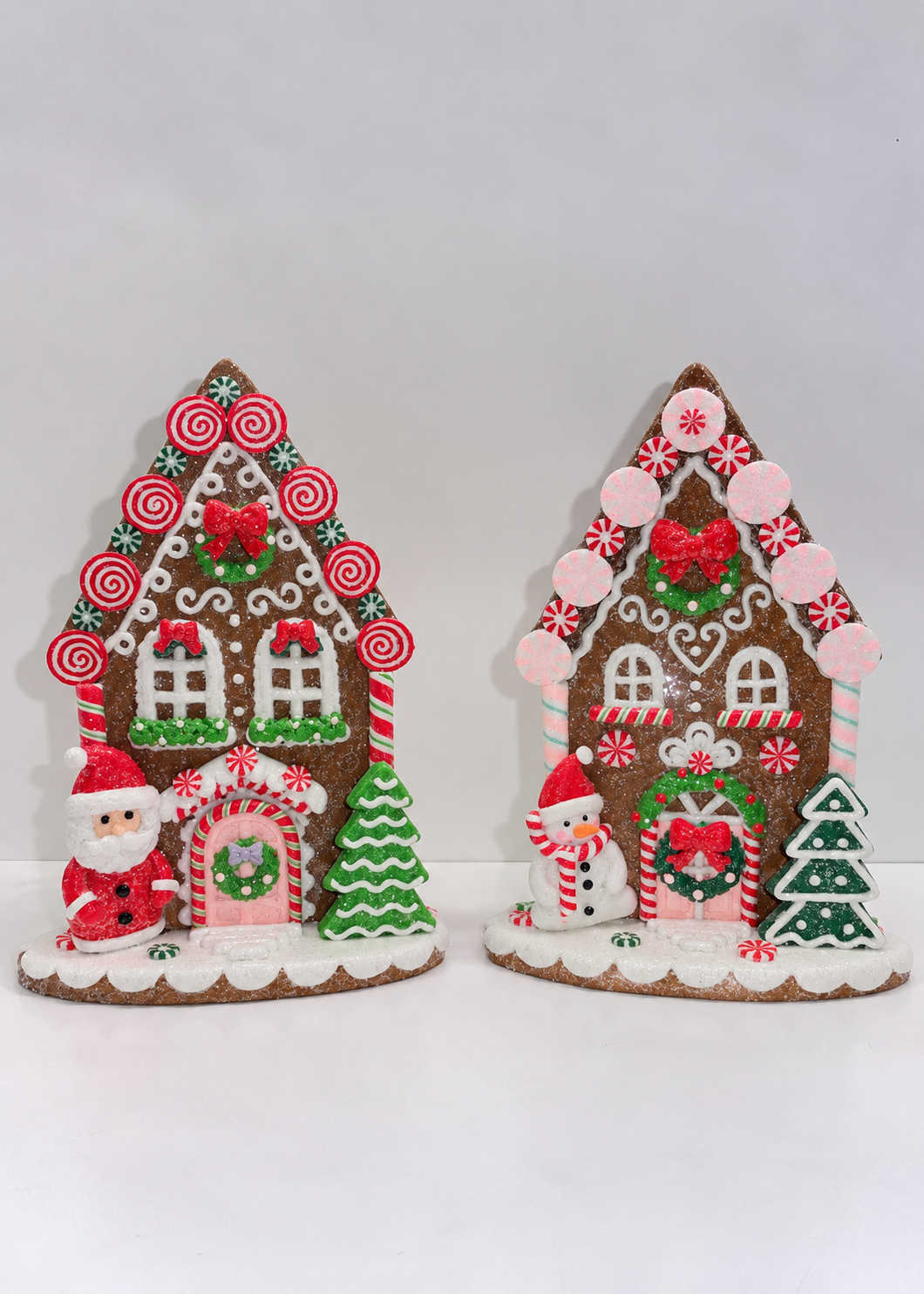Two decorative gingerbread house ornaments with festive holiday details, including candy canes, wreaths, a Santa Claus figure, and a snowman, displayed against a plain white background.