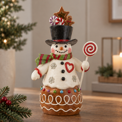 A festive Christmas snowman figurine standing on a decorated gingerbread base, placed on a wooden table in a warmly lit indoor setting with holiday greenery and candles in the background.