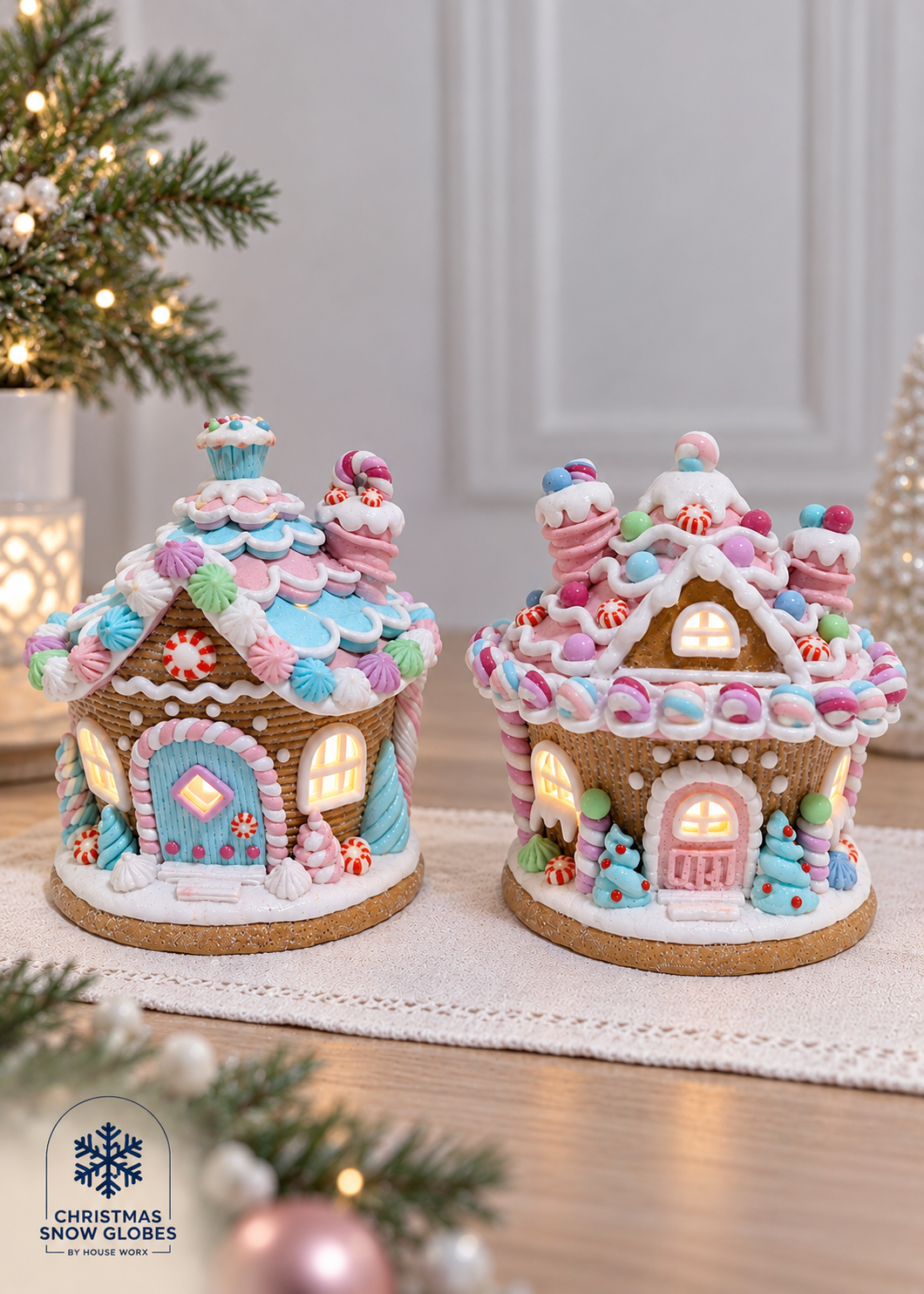 Two decorative gingerbread houses with colorful icing-like details and warm glowing windows, displayed on a tabletop in a holiday setting. A Christmas tree and soft home decor are blurred in the background.