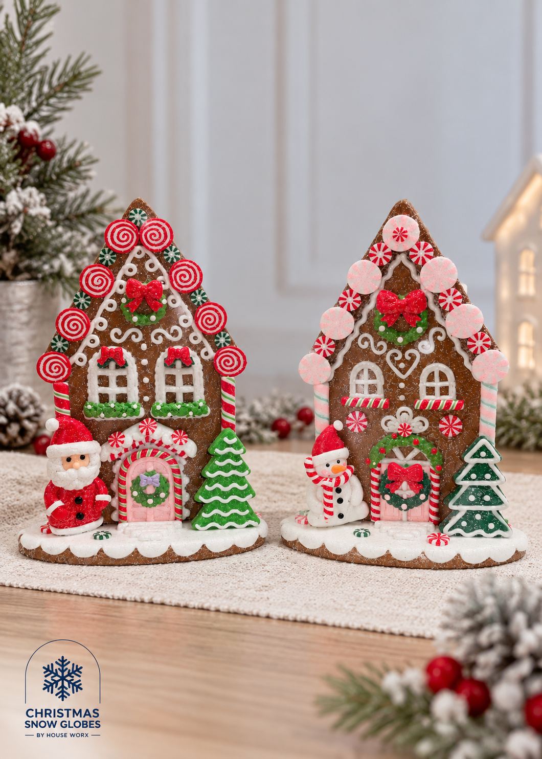 Two decorated gingerbread houses with festive holiday details, including candy canes, snow globes, a Santa Claus figure, and a snowman, displayed on a table runner with Christmas decorations in the background.