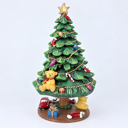A decorative miniature Christmas tree figurine with a gold star on top, green textured branches, gold bead garlands, colorful ornaments, a yellow teddy bear, candy canes, presents, a red car, and a small base on a white background.