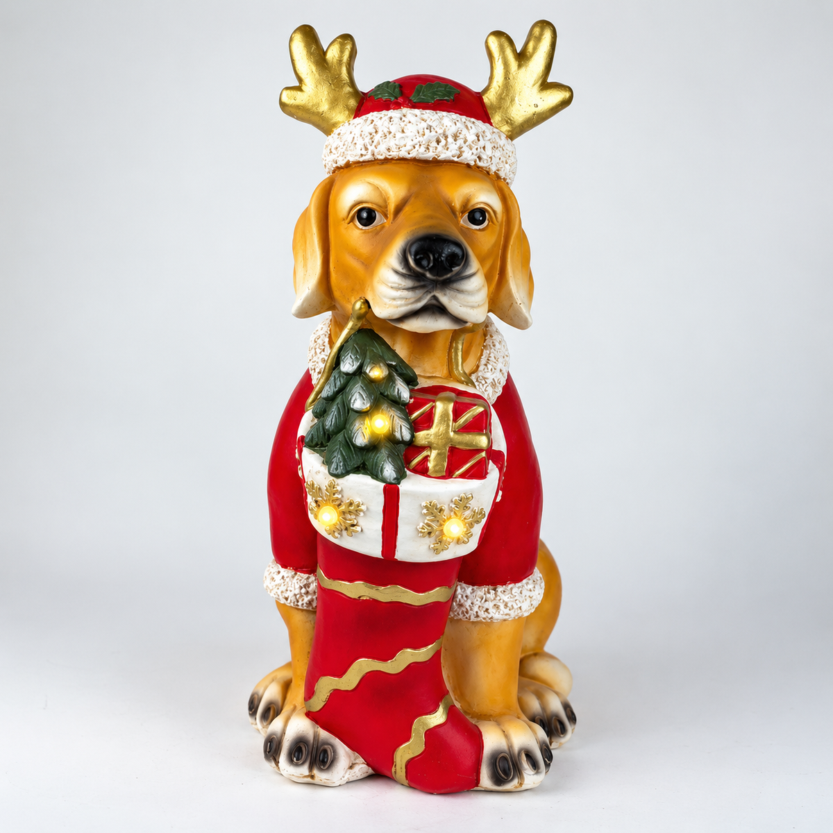 A decorative figurine of a golden-brown dog wearing a red Santa hat with gold antlers and a red Christmas sweater with a stocking, set against a plain light gray background.