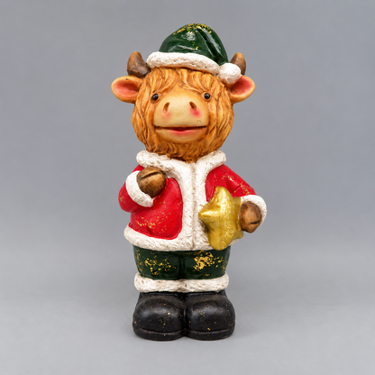 A festive decorative figurine of a cow dressed in a Santa-style outfit, featuring a green hat with white trim, a red jacket with white faux-fur trim, dark green pants with gold glitter accents, and black boots, set against a solid gray background.