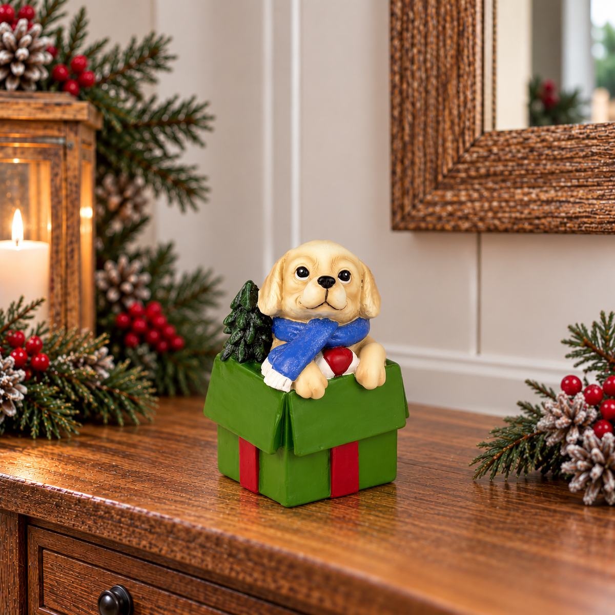A decorative figurine of a cream-colored puppy wearing a blue scarf and sitting in a green gift box with red ribbon, displayed on a wooden console table with holiday decorations.