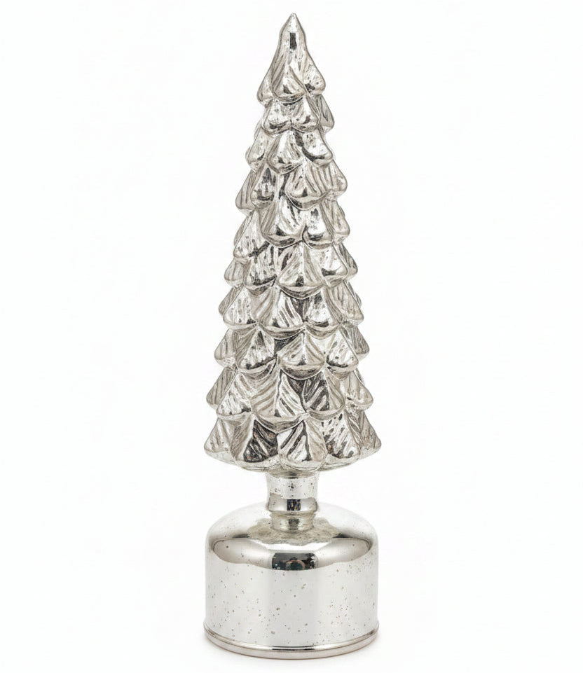 A small metallic silver Christmas tree ornament with a tiered textured design on a clear round base, standing on a kitchen countertop with a white sheet of paper behind it.