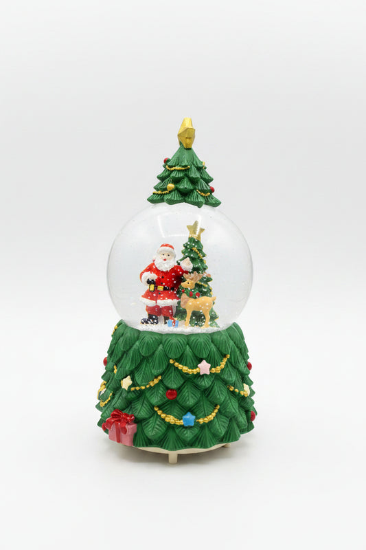 A Christmas-themed snow globe figurine with Santa Claus, a small Christmas tree, reindeer, and a decorated green base on a dark countertop.