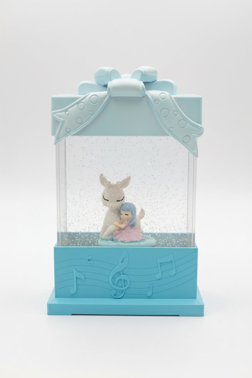 A light blue gift box snow globe figurine featuring a white deer and a small blue-haired girl sitting inside, with glittery snow falling inside a clear box on a speckled dark countertop.