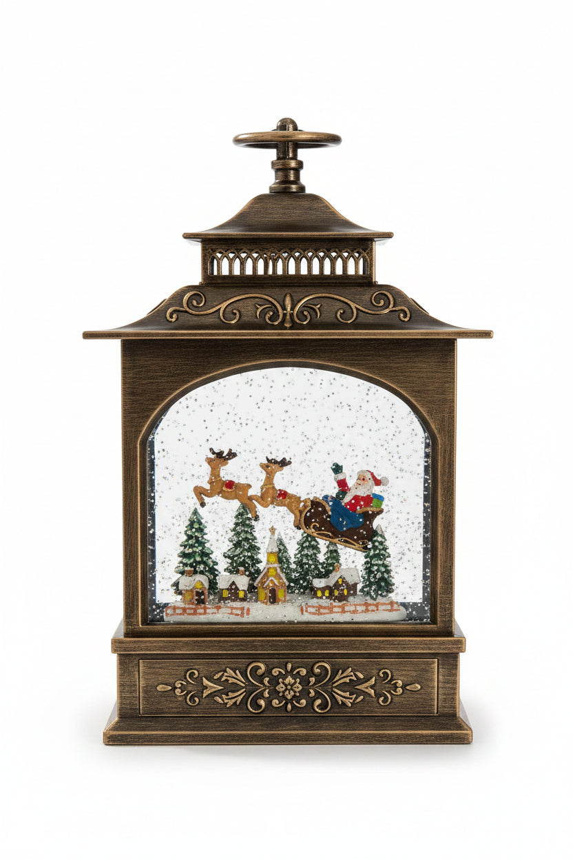 A decorative tabletop lantern-style Christmas ornament with an antique bronze finish and a snow globe scene inside featuring Santa Claus, reindeer, trees, and small houses, shown on a granite countertop.