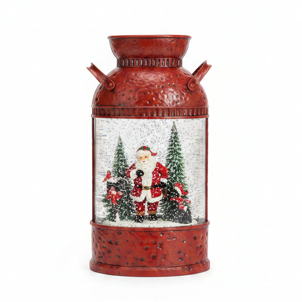 A red metal milk-can-shaped Christmas lantern with Santa Claus and snow figures inside a clear globe, set on a dark granite countertop with a white card behind it.