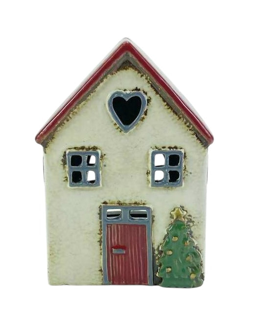 A small decorative house-shaped ceramic ornament with a cream-colored body, red roof and door, gray window frames, and a green Christmas tree at the side, shown on a plain white background.