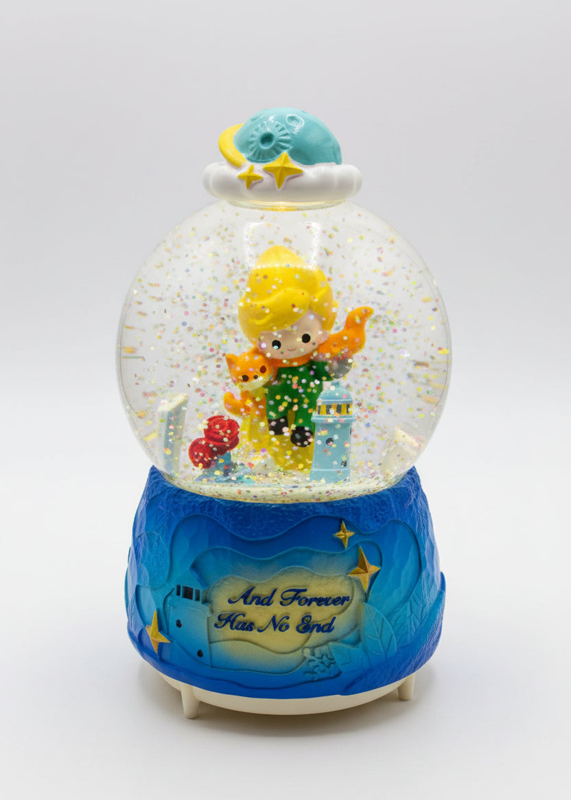 A decorative snow globe figurine with a blue base and a character inside a clear globe filled with glitter, set on a dark countertop with a white box behind it.