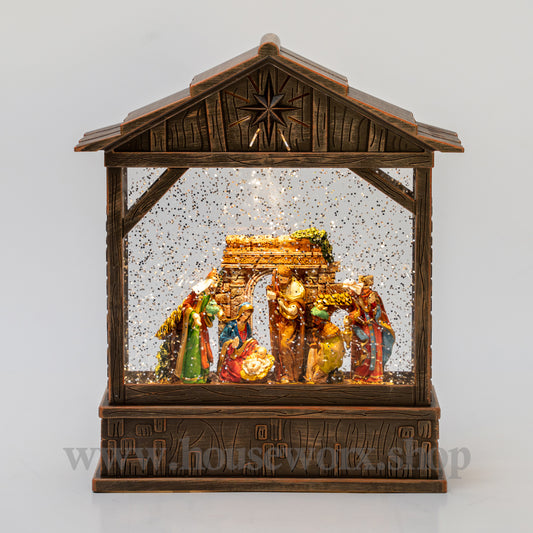 Decorative nativity scene in a wooden stable with snow effect on a white background. Christmas snow globe bronze