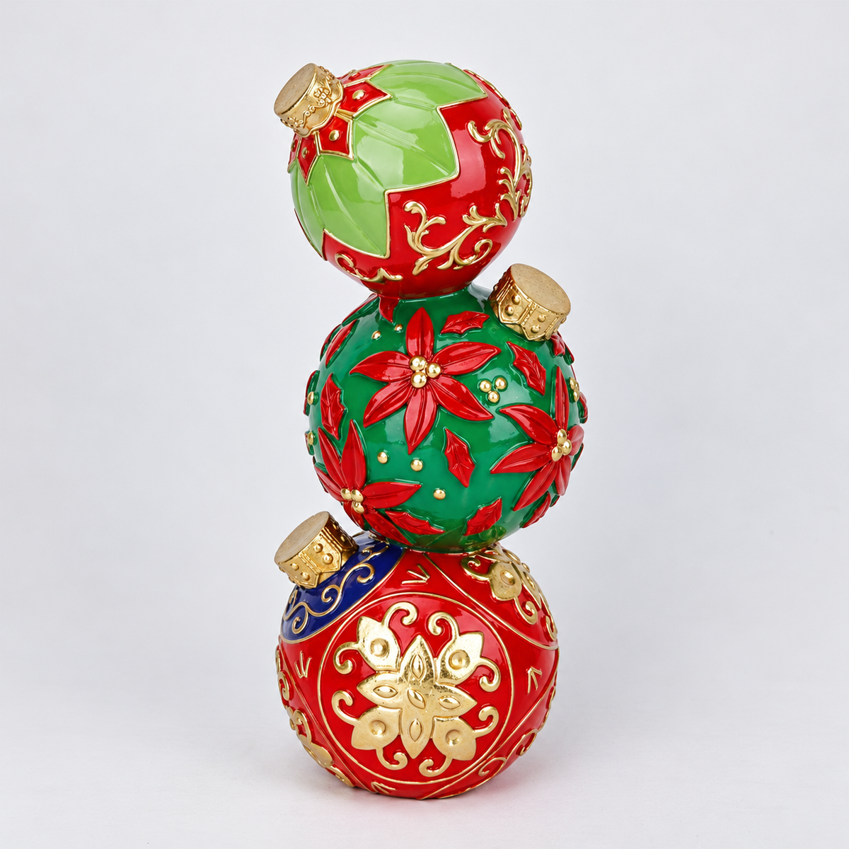 Three stacked Christmas ornaments in glossy red and green with gold decorative patterns and gold caps, photographed on a clean white background.