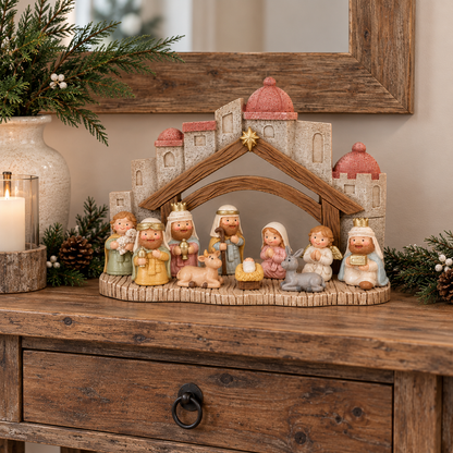 A rustic wooden nativity scene display on a wooden console table, featuring a stable backdrop with pink domes, a small gold star, and multiple painted figurines of the Holy Family, wise men, and angels, surrounded by holiday greenery and a lit candle.