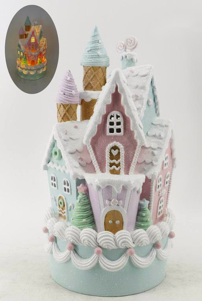 A decorative gingerbread-style castle ornament or cake topper with pastel pink, mint green, lavender, and white icing details, shown on a plain light background. A small oval inset at the upper left shows the item lit up from within.