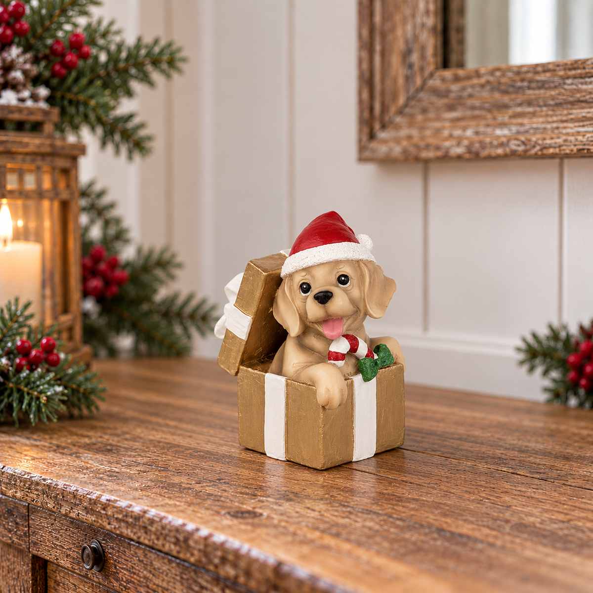 A decorative figurine of a golden retriever puppy sitting in an open gift box, wearing a red Santa hat and holding a candy cane, displayed on a wooden table with holiday decorations in the background.