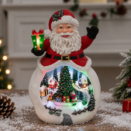 A Santa Claus snowman Christmas night light figurine with a glowing winter village scene inside, set on a tabletop with festive holiday decor in the background.