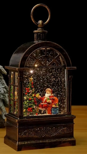 A dark bronze-finished decorative lantern with a Santa Claus snow globe scene inside, featuring a hanging loop on top, shown against a black background.