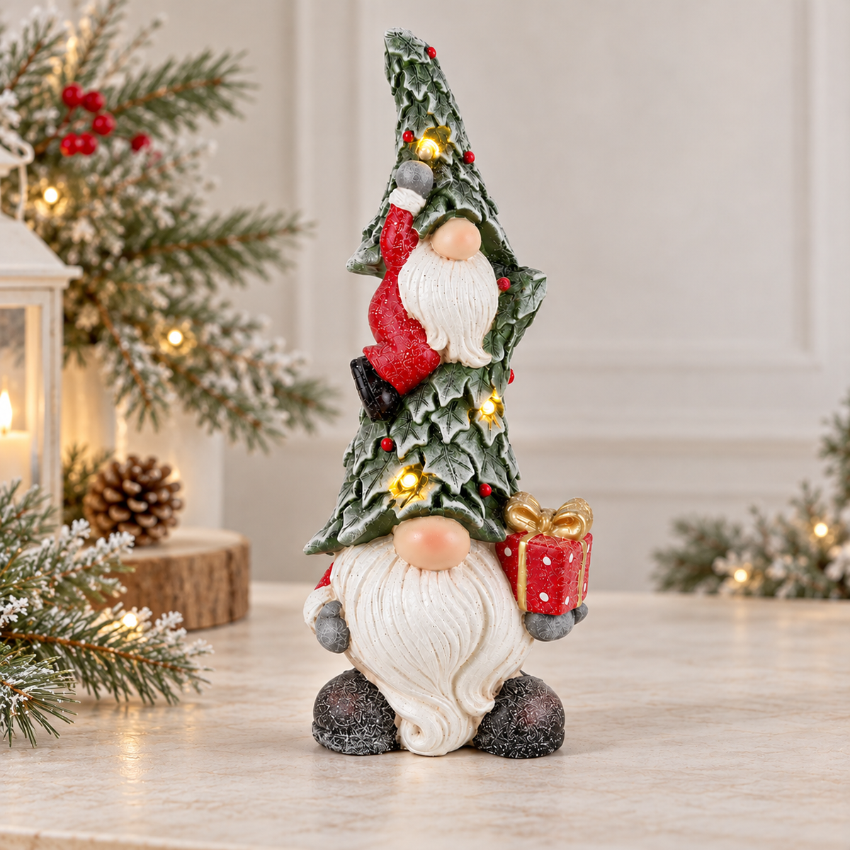 A Christmas gnome figurine stands on a light marble surface, wearing a tall green holly-patterned hat with red accents, a white beard, and holding a red gift box with gold details. The background is softly blurred with holiday lights, pine branches, and a lantern.