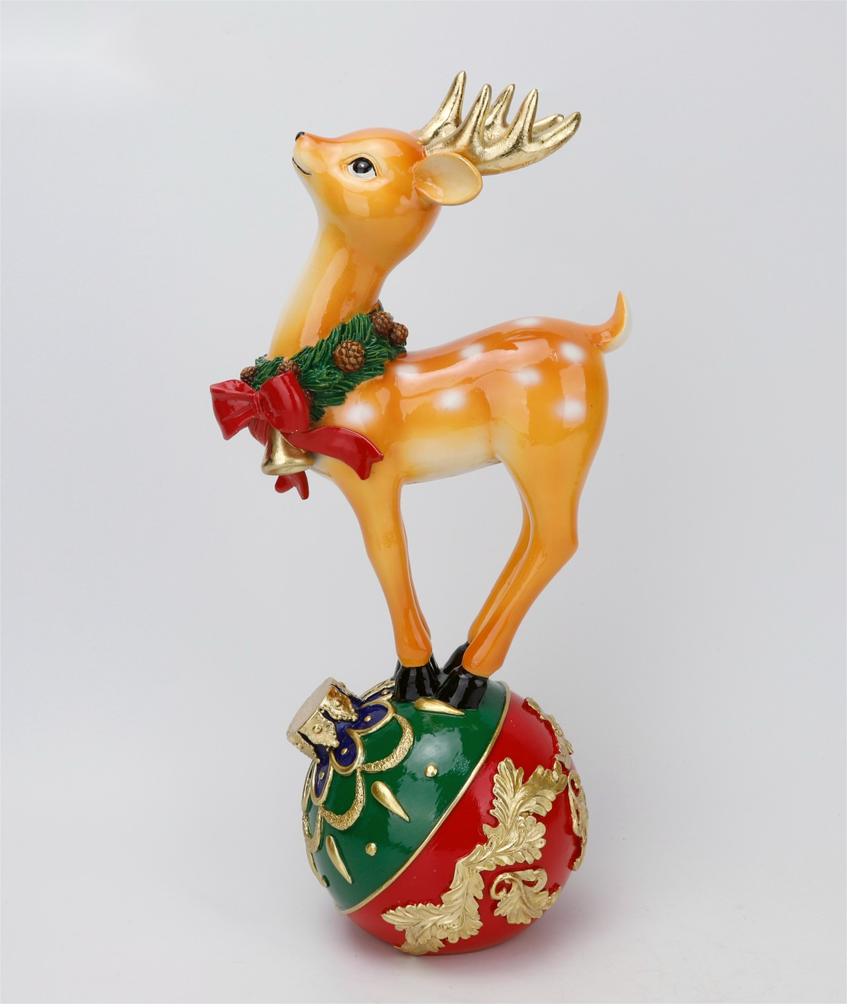 A festive Christmas ornament featuring a golden deer with white spots standing on a red and green decorated ball, wearing a green wreath with a red bow.