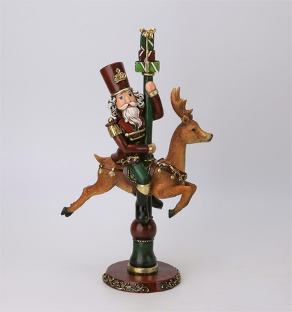 A hand-painted Christmas nutcracker figurine riding a brown stag, holding a green staff with gold ornaments and a gift box on top, mounted on a round decorative base against a light gray background.