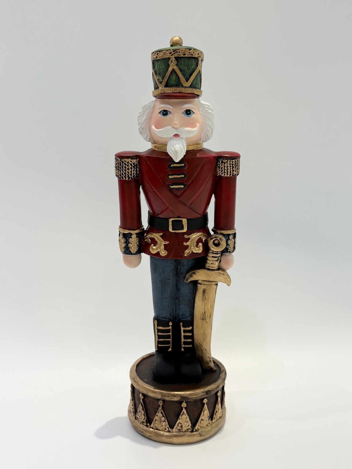 A traditional wooden nutcracker figurine dressed in a red military uniform with gold trim, blue pants, and a green and gold hat, holding a sword and standing on a decorative base.