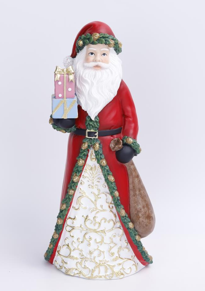 A Santa Claus figurine holding a sack and wrapped presents, dressed in a red coat with a white patterned skirt, green garlands, and a gold belt, photographed against a light gray studio background.