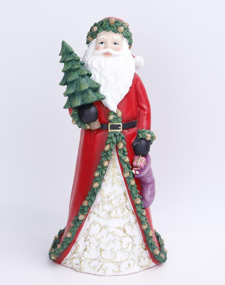 A Santa Claus figurine holding a small green Christmas tree, wearing a red coat with a white patterned skirt, green garland trim, and black gloves, photographed against a light gray studio background.