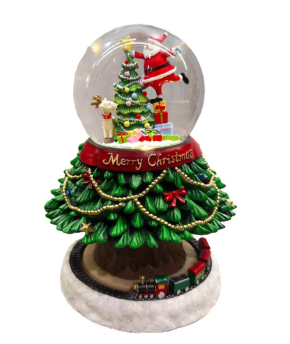 A festive Christmas snow globe figurine featuring a decorated green Christmas tree on a round base with a small train, Santa Claus inside a clear globe, and a red band reading 'Merry Christmas'.
