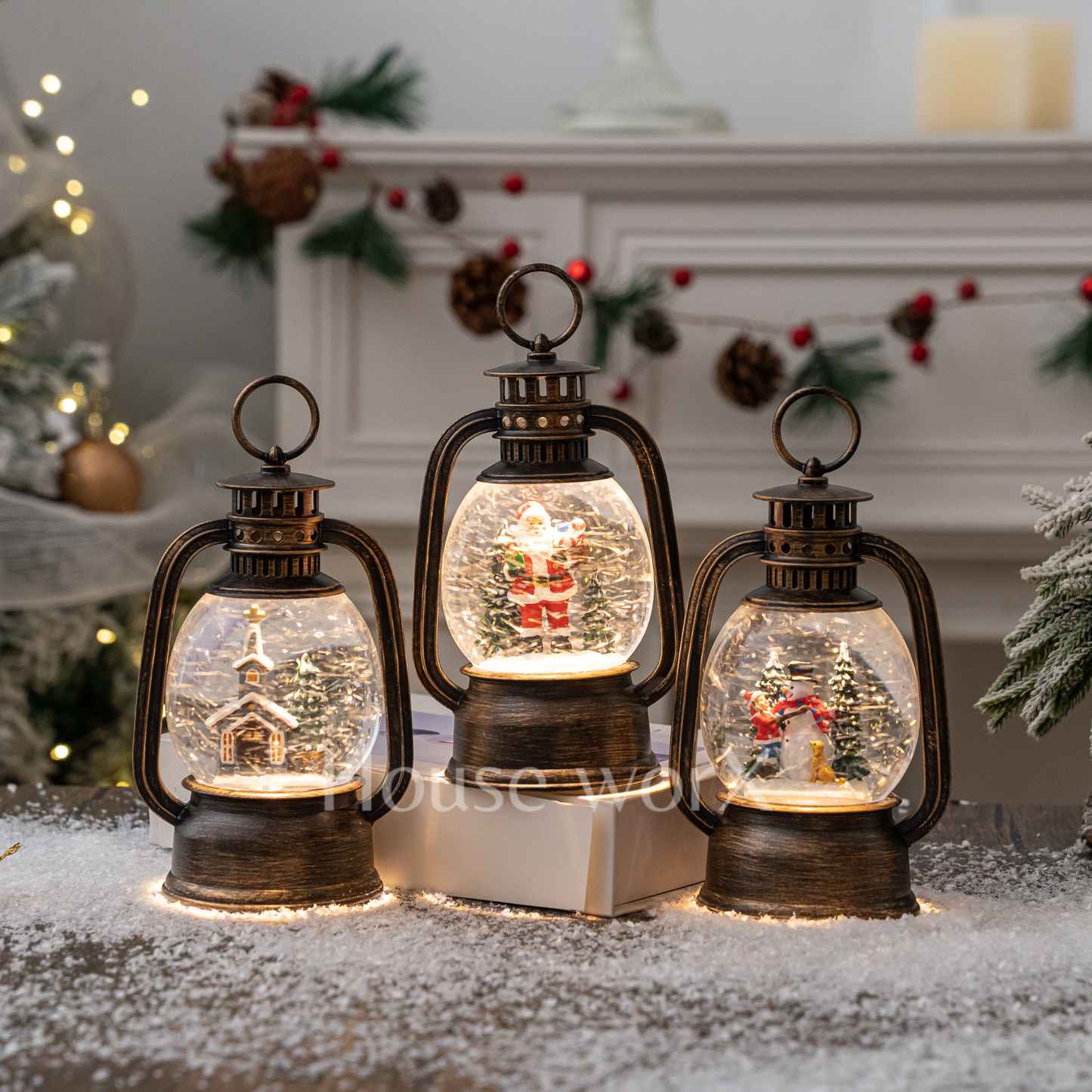 Three decorative lanterns with Christmas scenes inside, placed on a snowy surface.