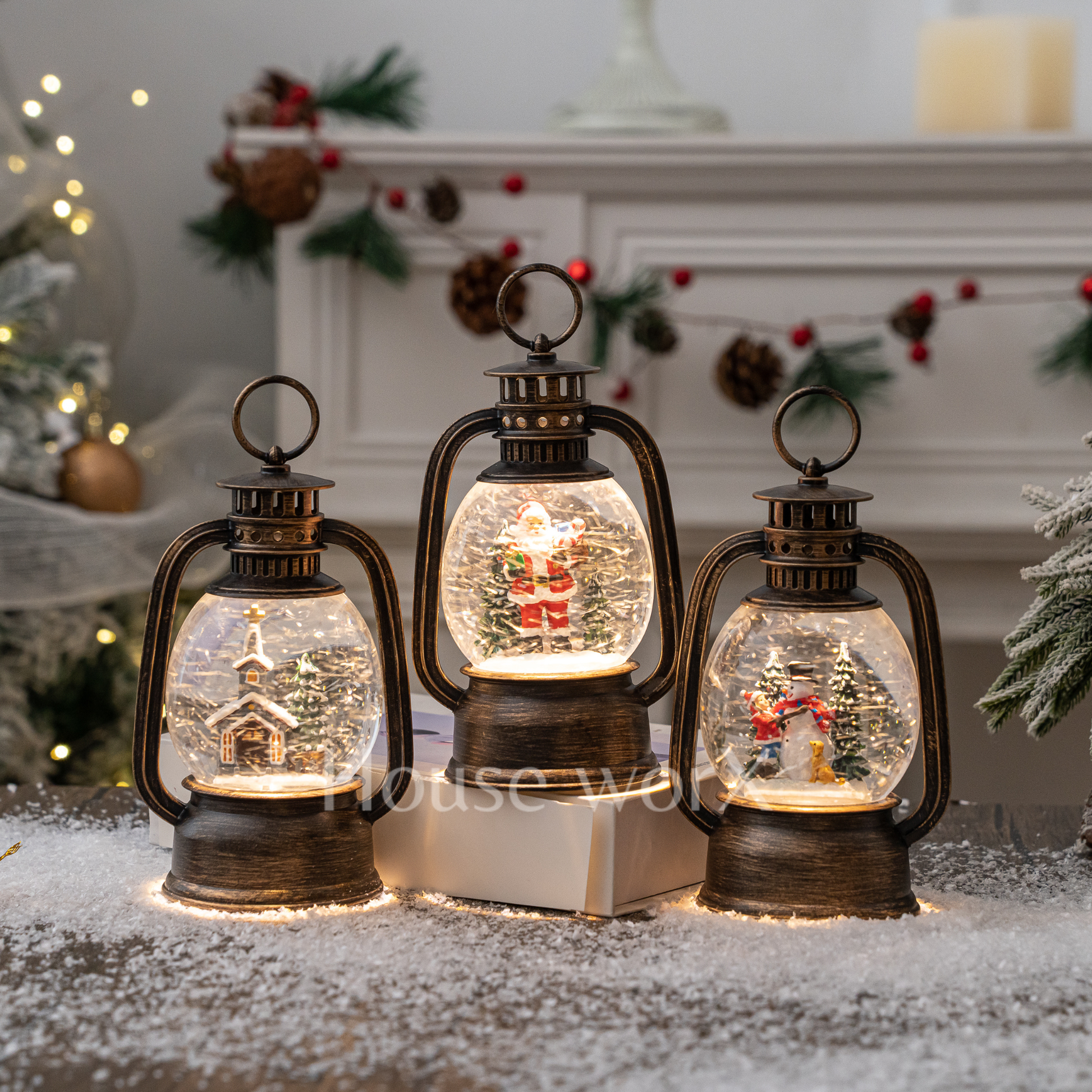Three decorative lanterns with Christmas scenes inside, placed on a snowy surface.