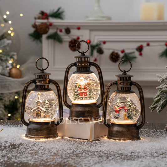 Three decorative lanterns with Christmas scenes inside, placed on a snowy surface.