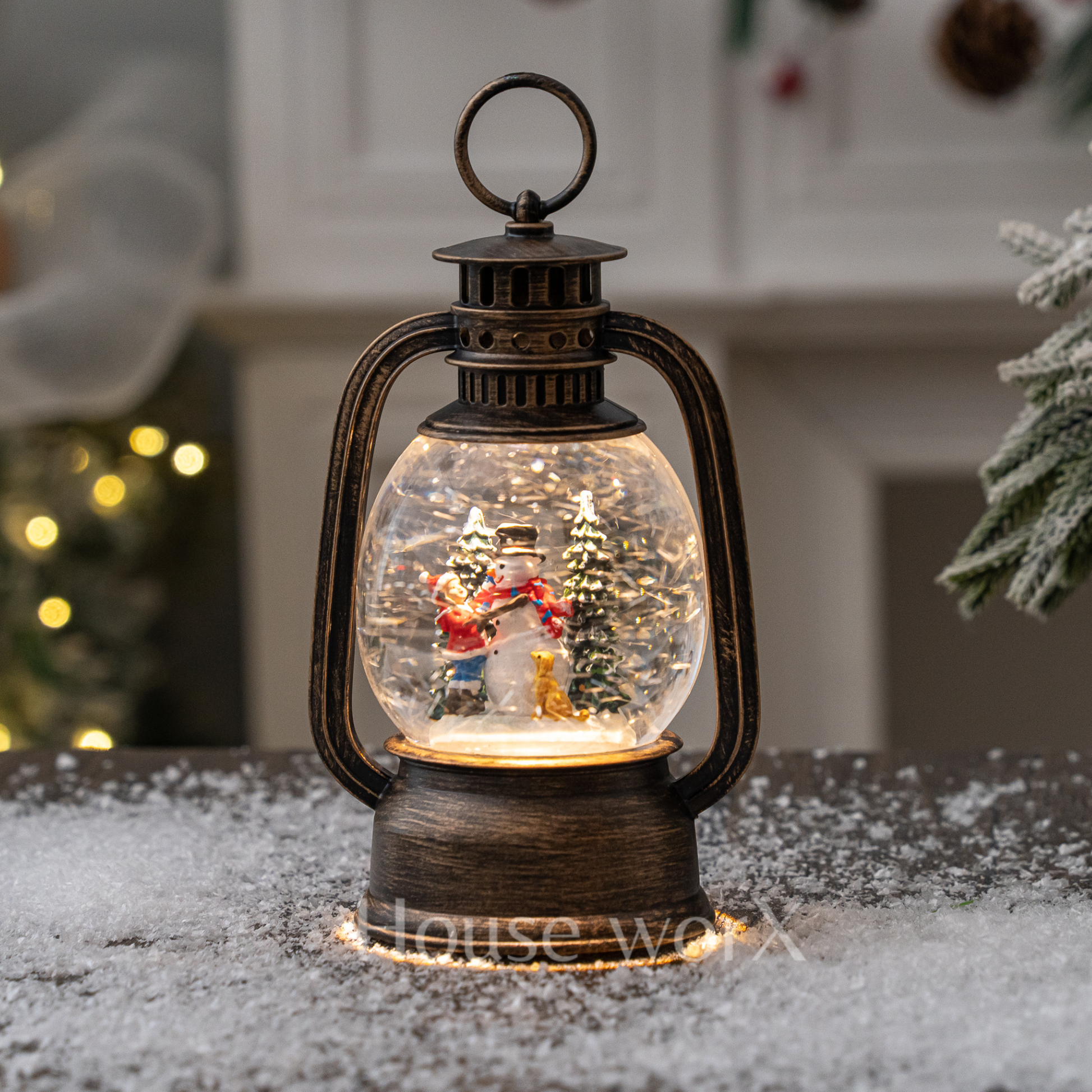Decorative lantern snow globe with Christmas scene inside, placed on a snowy surface.