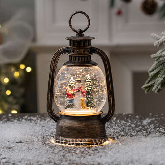Decorative lantern snow globe with Christmas scene inside, placed on a snowy surface.