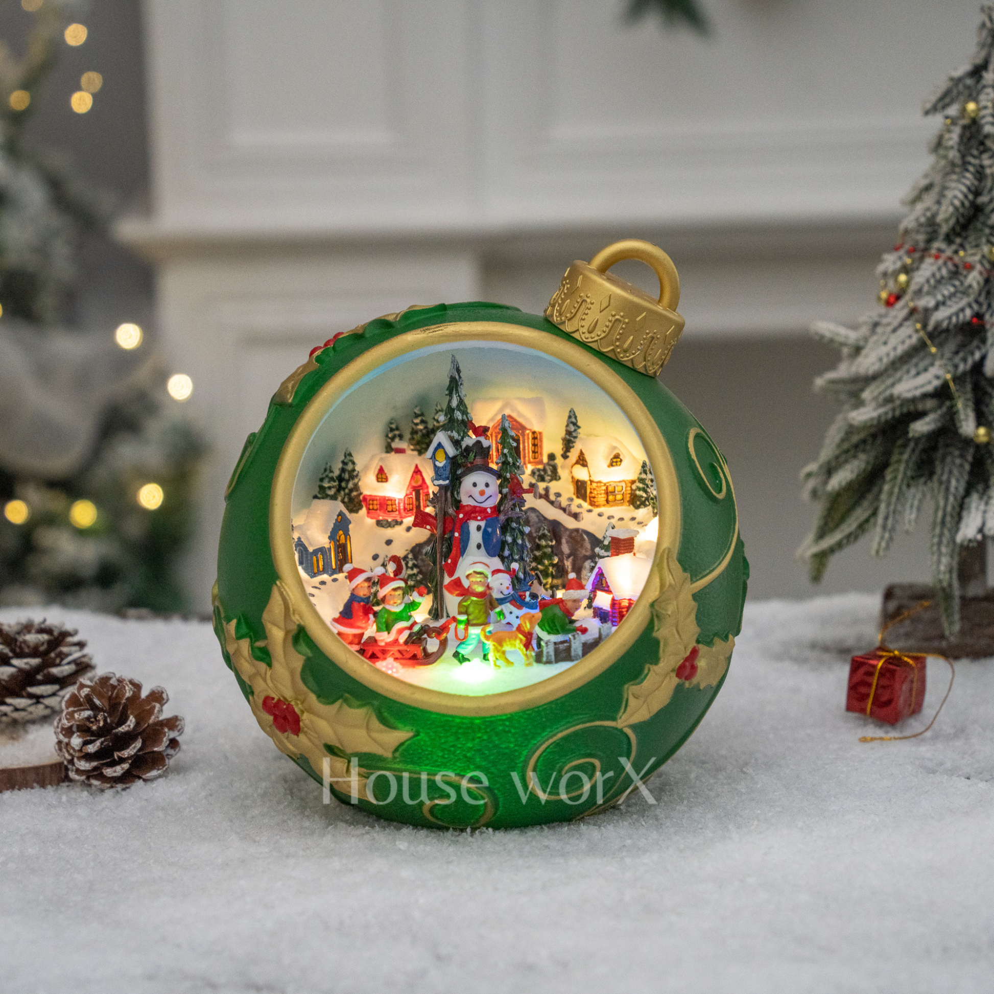 Decorative Christmas ornament with a snowman and village scene inside, on a snowy surface with trees and lights in the background.