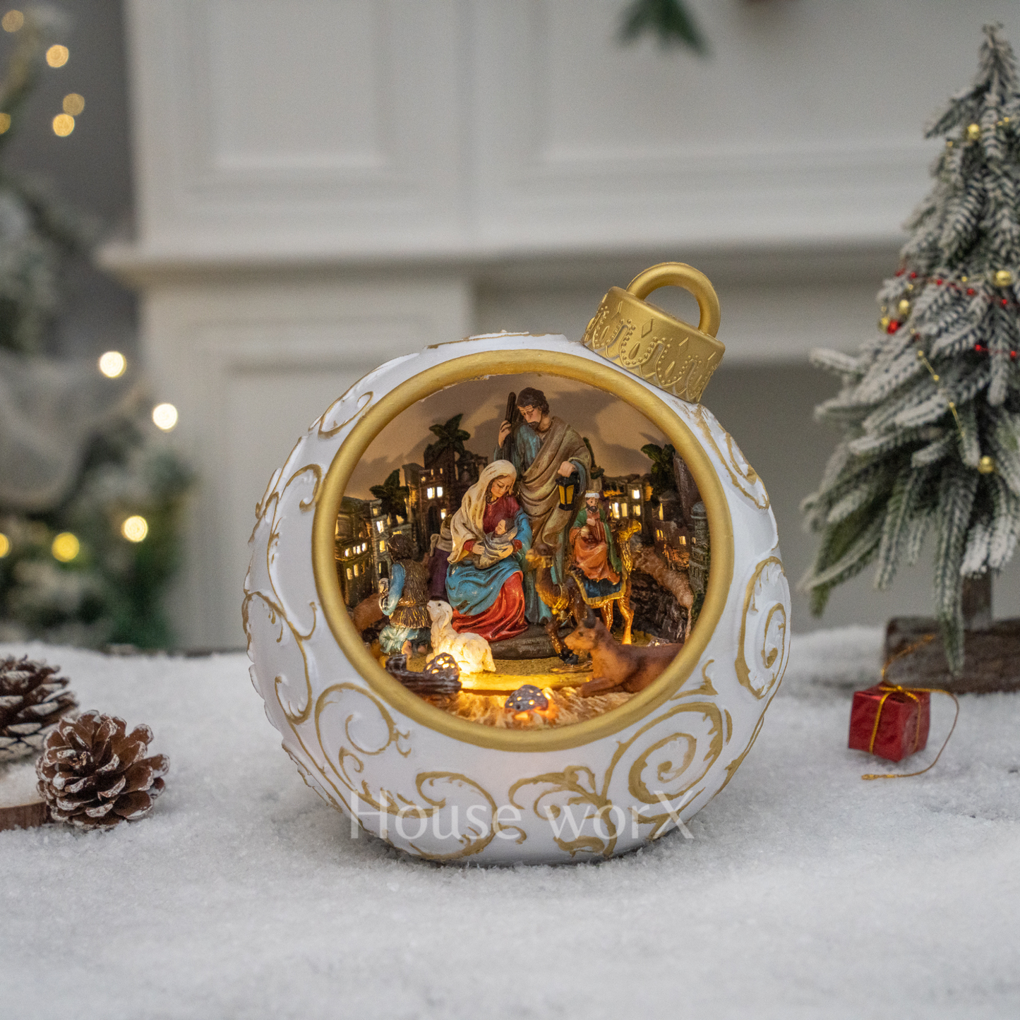 Decorative Christmas ornament with nativity scene inside, placed on a snowy surface with festive background.