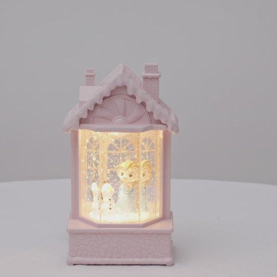 Decorative lamp shaped like a house with a warm glow on a light gray snow   video