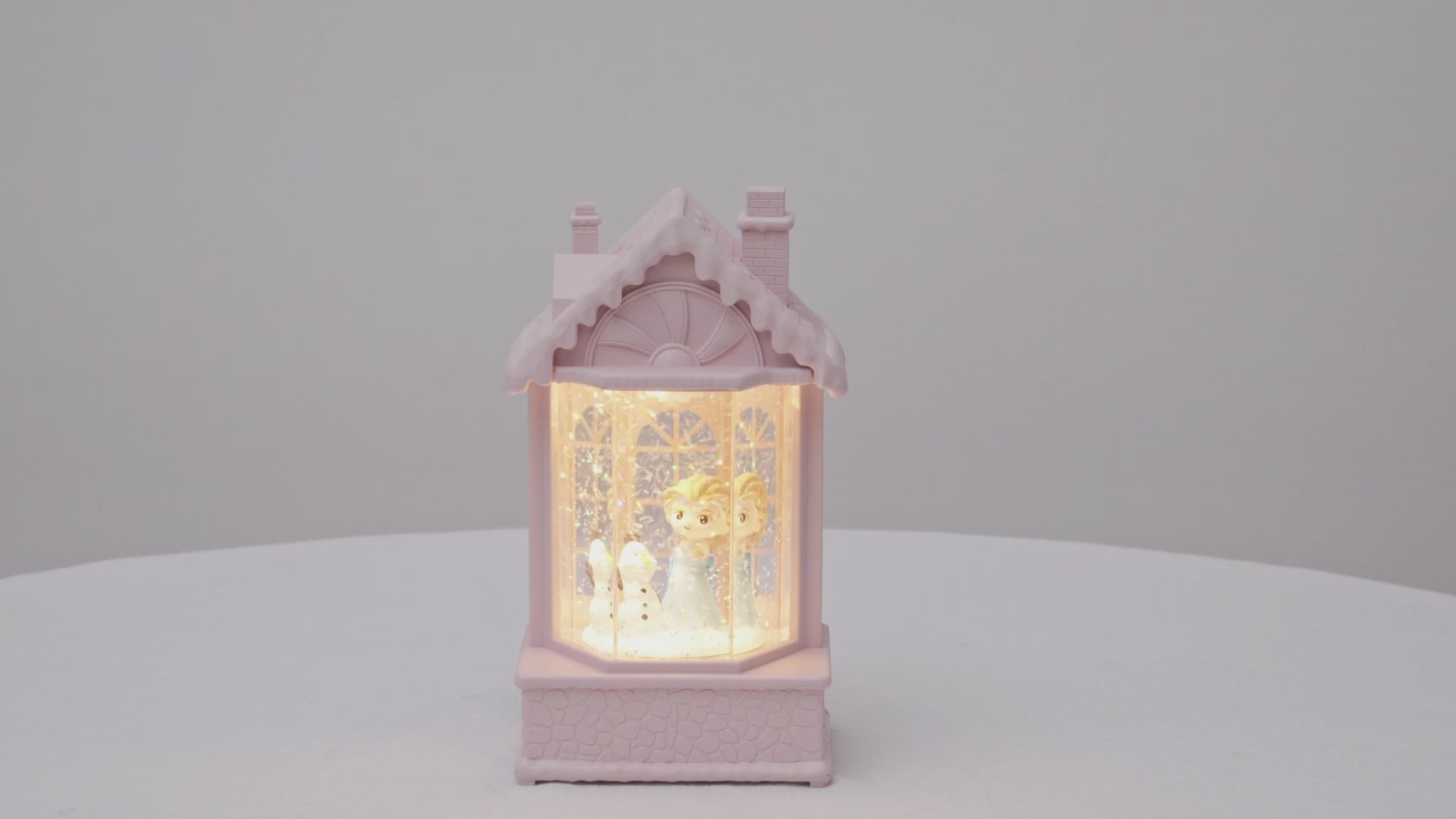 Decorative lamp shaped like a house with a warm glow on a light gray snow   video