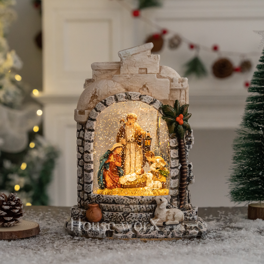 Decorative nativity scene in a snow globe with lights, placed on a surface with a festive background.